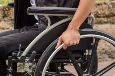 Close-up of male hand on wheel of wheelchair during walk in park